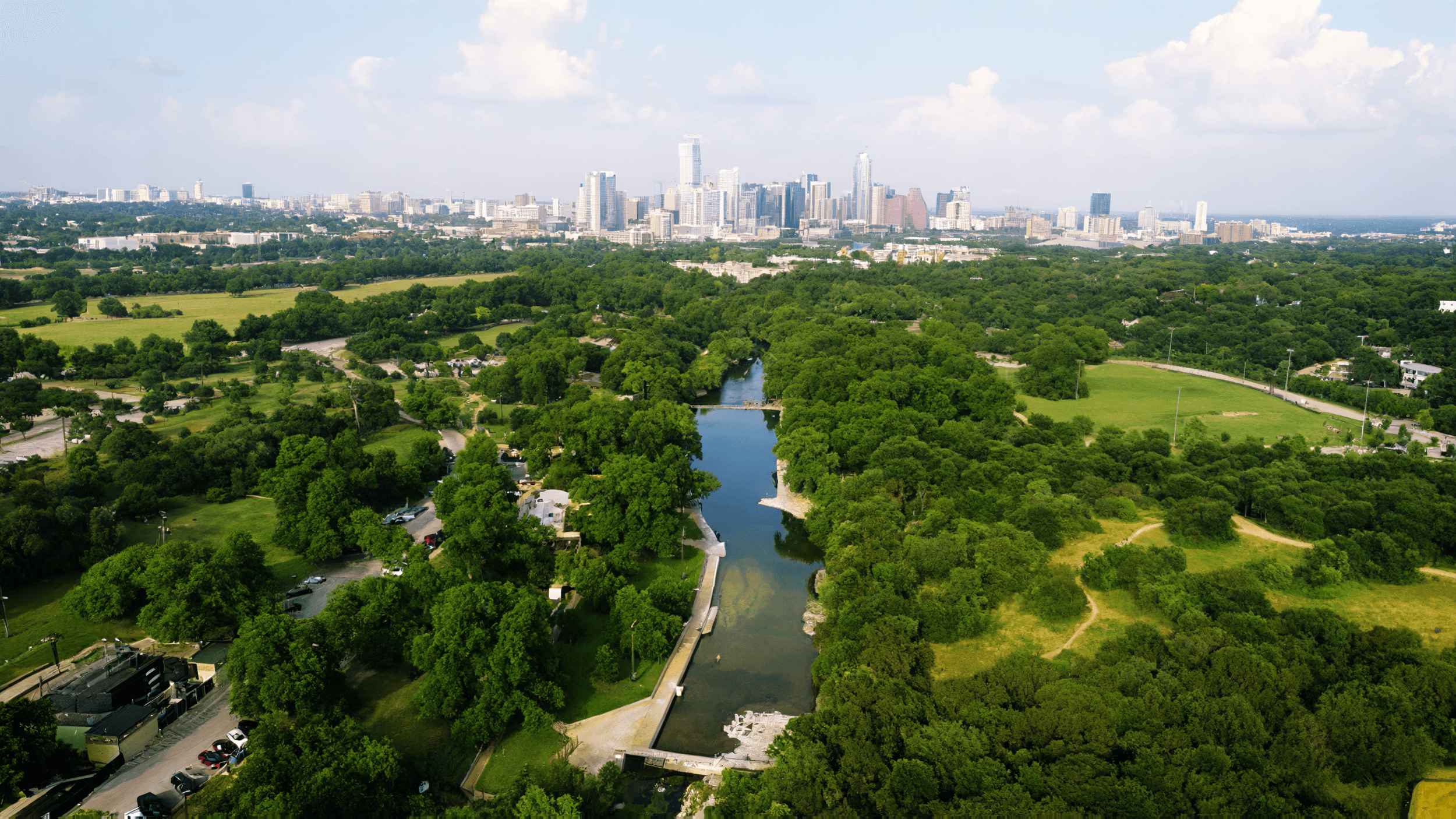 Aerial view of Barton Creek winding through Zilker Park with the downtown Austin skyline beyond