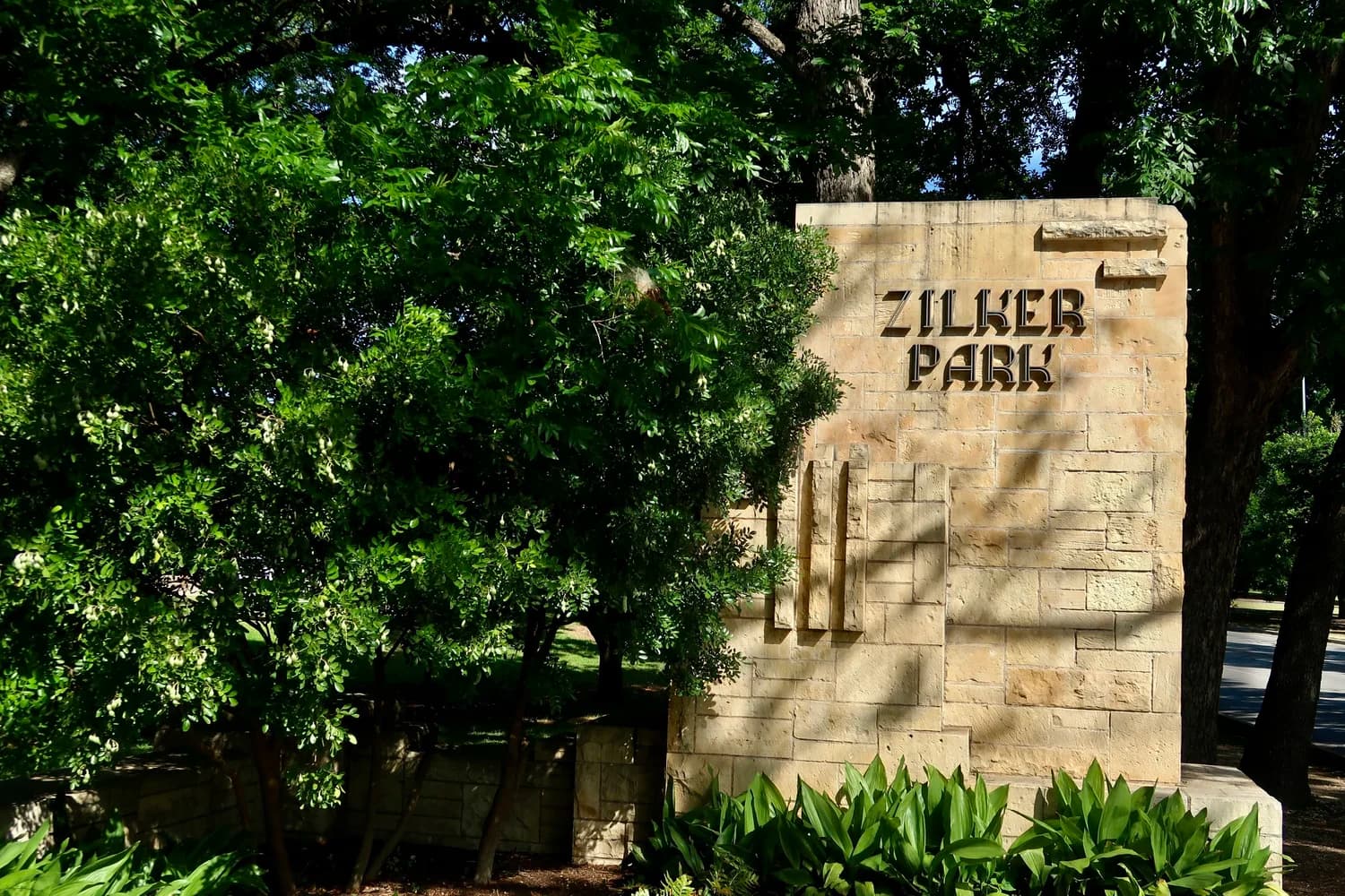 The historic limestone Zilker Park entrance sign framed by trees