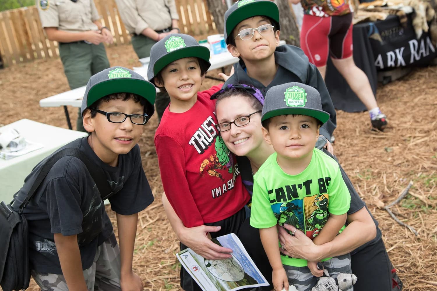 Children in junior park ranger caps posing with a volunteer at a park event
