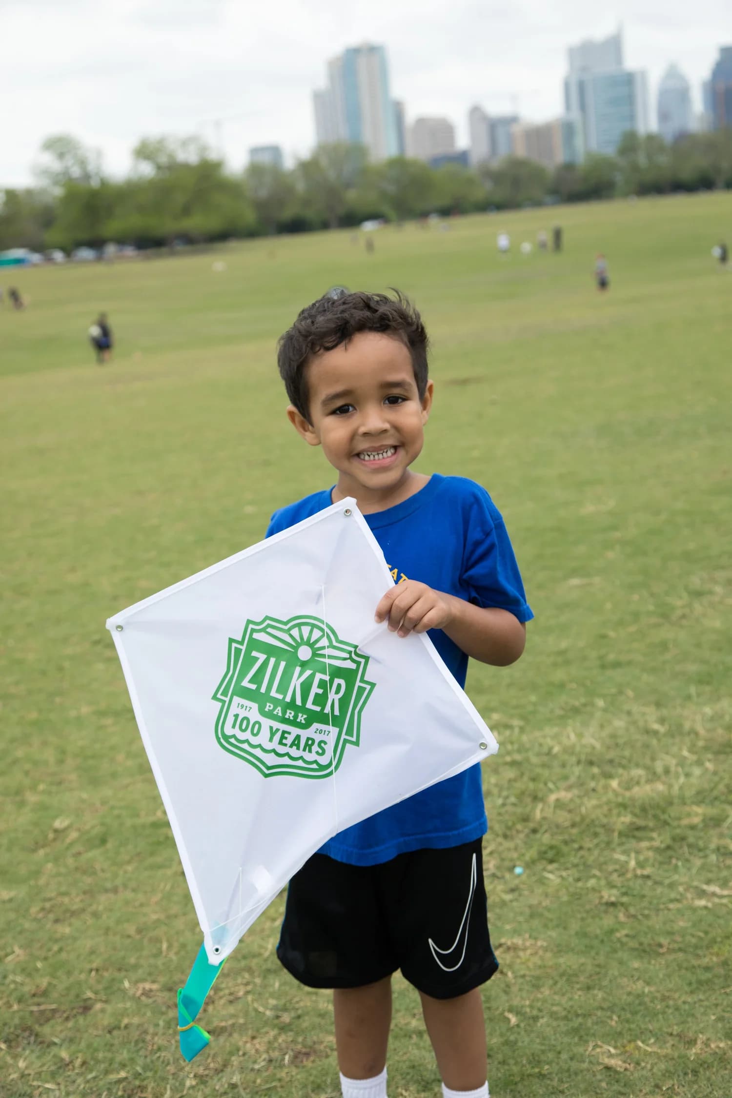 A young boy holding a Zilker Park 100 Years kite on the great lawn
