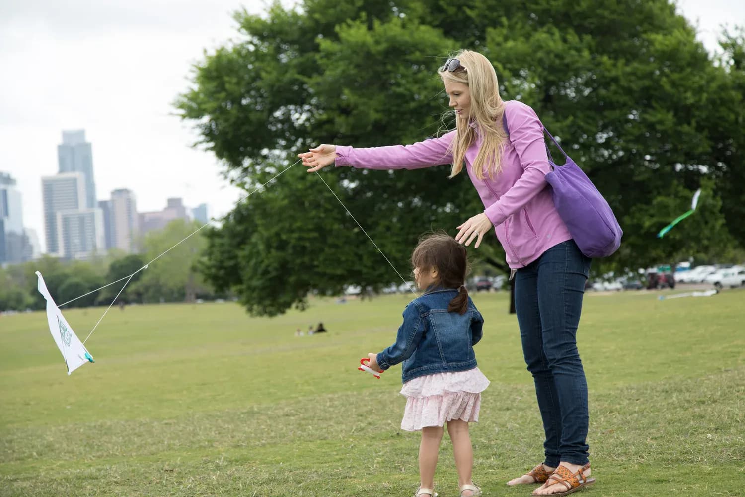 A parent and child flying a kite on the Great Lawn with the Austin skyline behind