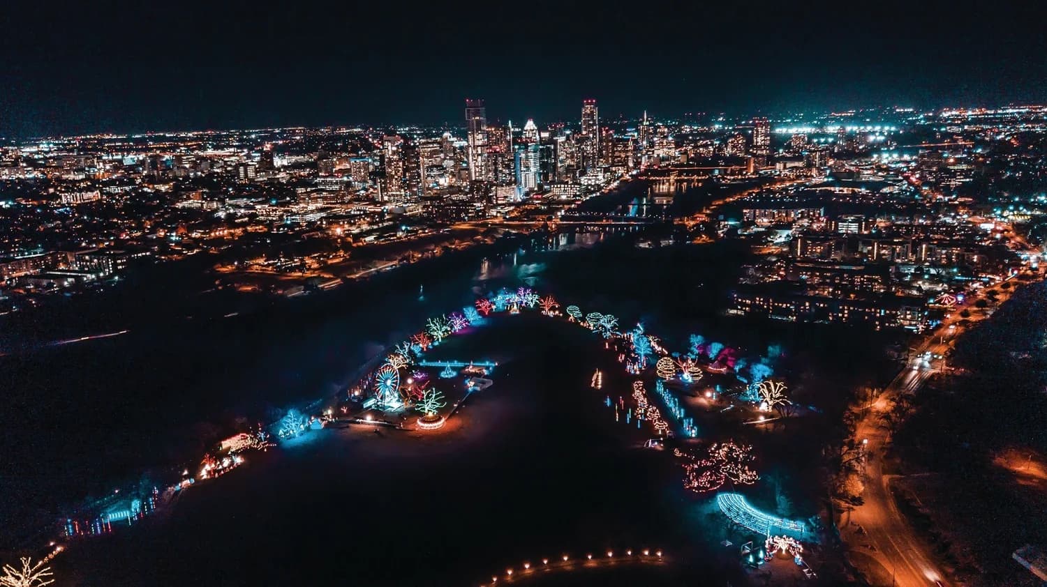 Aerial night view of the Trail of Lights glowing within the park beside the city