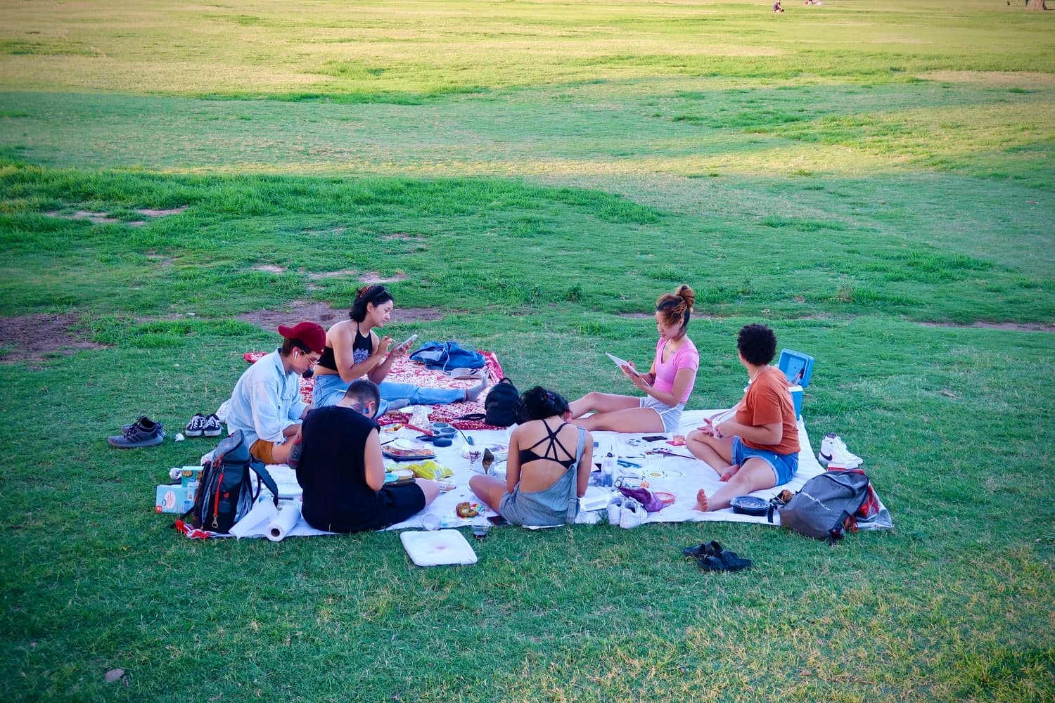 Friends sharing a picnic on a blanket on the Great Lawn at golden hour in Zilker Park