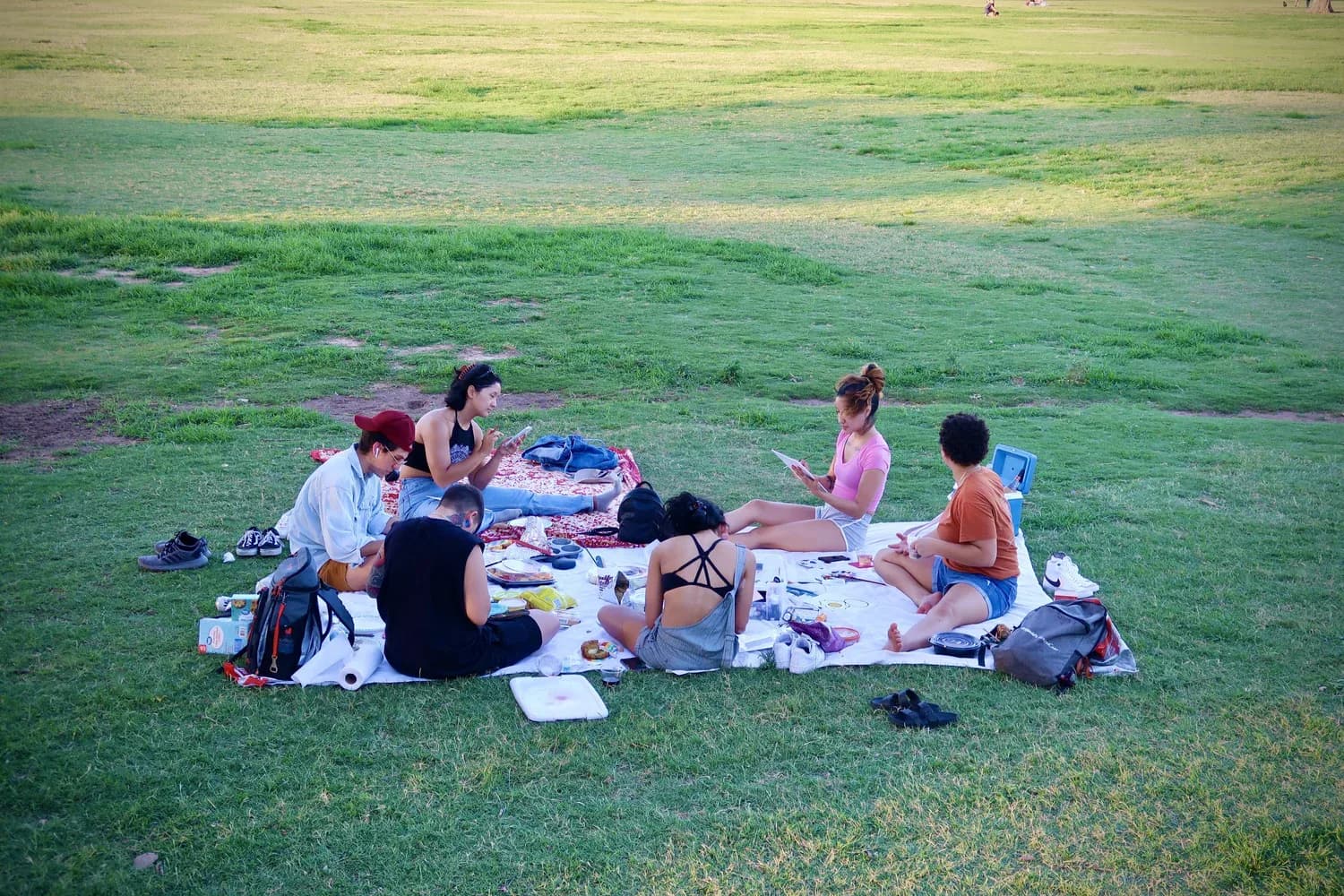 Friends sharing a picnic on a blanket on the Great Lawn at golden hour in Zilker Park
