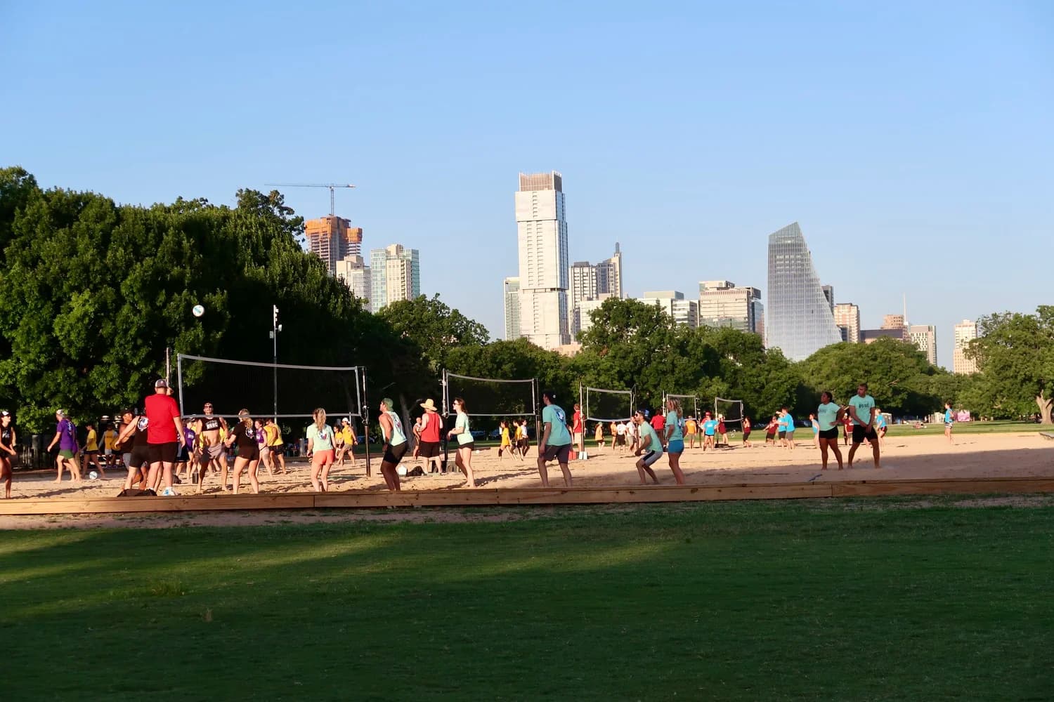 People playing volleyball on the sand courts at Zilker Park with the downtown Austin skyline behind