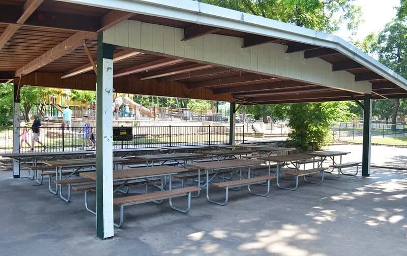 The covered picnic shelter with rows of picnic tables and a playground just beyond at Zilker Park
