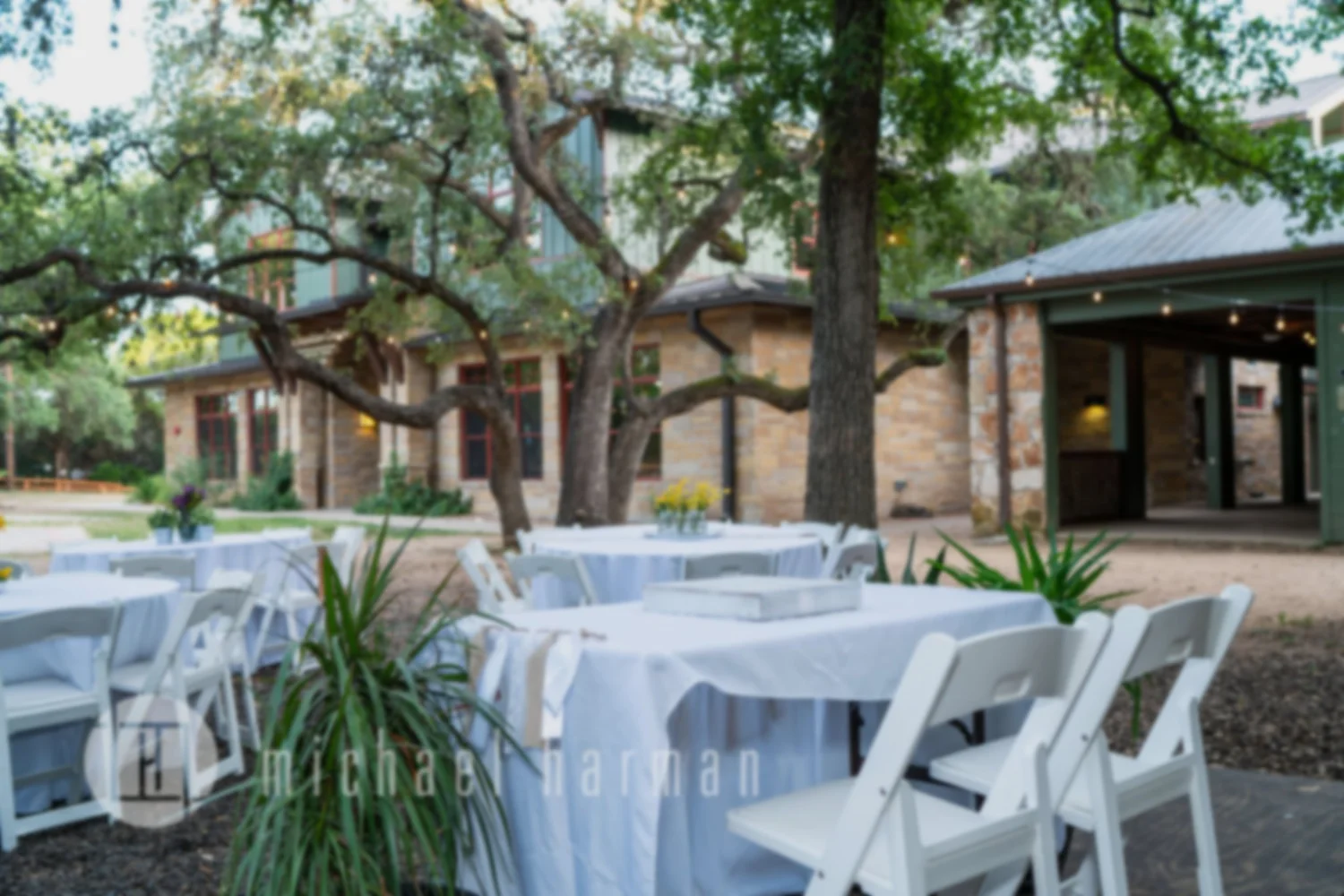 White-linen reception tables set under live oaks beside a Hill Country stone venue at Zilker Park